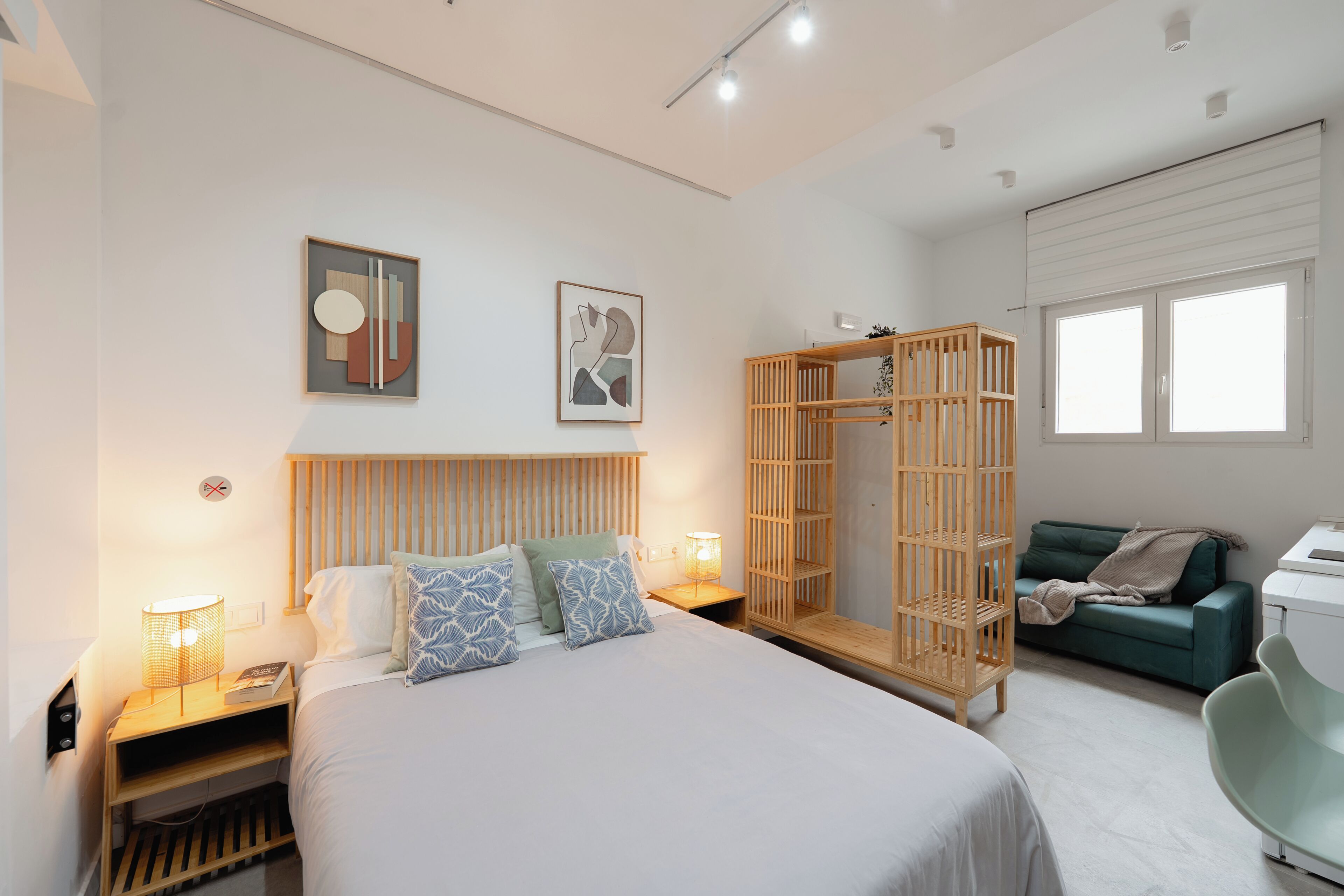 A modern bedroom with a bed, bedside lamps, a wooden wardrobe, a green sofa, and a desk.