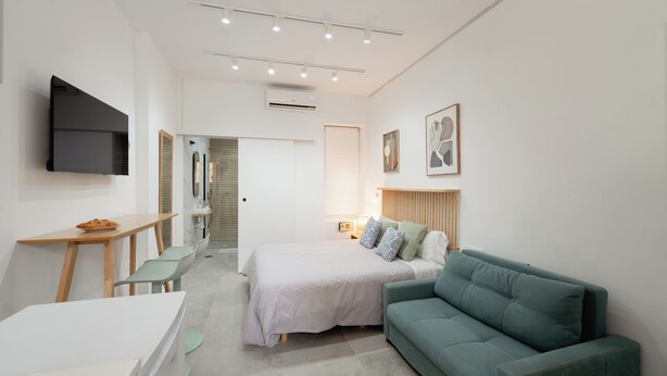 A modern hotel room with a bed, a green sofa, a desk with a chair, a flat-screen TV, and a framed picture on the wall. - Mini Apartment Baélia Casa Íbera (Alicante)