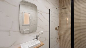 A bathroom with a marble wall, a sink with a mirror, and a shower with a glass door. - Mini Apartment Baélia Casa Íbera (Alicante)