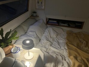 Ein Bett mit weißer Bettwäsche, eine Nachttischlampe, eine Pflanze und ein Fenster.