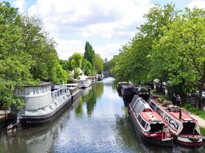 A narrow canal with boats docked on both sides, surrounded by lush green trees. - House Sleeps 2 With Lakeside Views (London)
