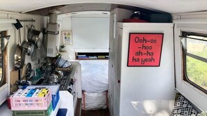 Een kleine keuken met een fornuis, pannen en een bordje met een vrolijke boodschap.