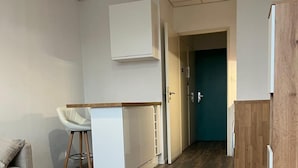 Moderni sisustus, jossa on puulattia, valkoinen työpöytä, valkoinen tuoli ja pieni keittiöalue.