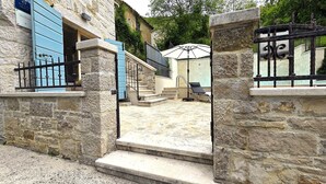 A stone building with a blue door, a staircase leading to a covered outdoor area, and a black metal gate. - CROGO Casa Gradinje-Holiday Home-Istria-Motovun (Gradinje)