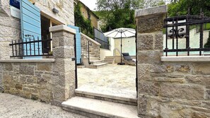 A stone building with a blue door, a staircase leading to a covered outdoor area, and a black metal gate.