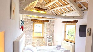 A bedroom with a sloped ceiling, a bed, a stone wall, and a window. - CROGO Casa Gradinje-Holiday Home-Istria-Motovun (Gradinje)
