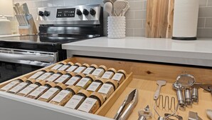 A kitchen with a stove, a white countertop, and a wooden spice rack.