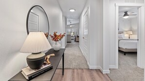 A hallway with a mirror, a lamp, a table with a book, and a vase with dried flowers.