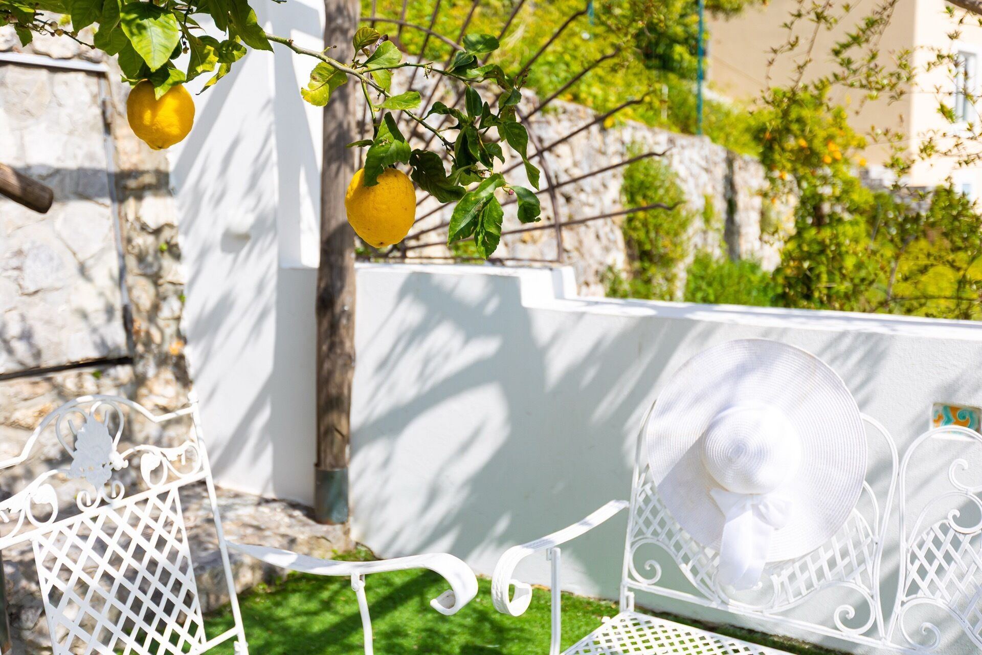 Une chaise en métal blanc avec un coussin, une table en métal blanc et une clôture en métal blanc ornée d’un citron suspendu.