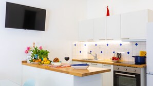 Una cocina moderna con armarios blancos, encimera de madera, horno integrado y televisor montado en la pared.