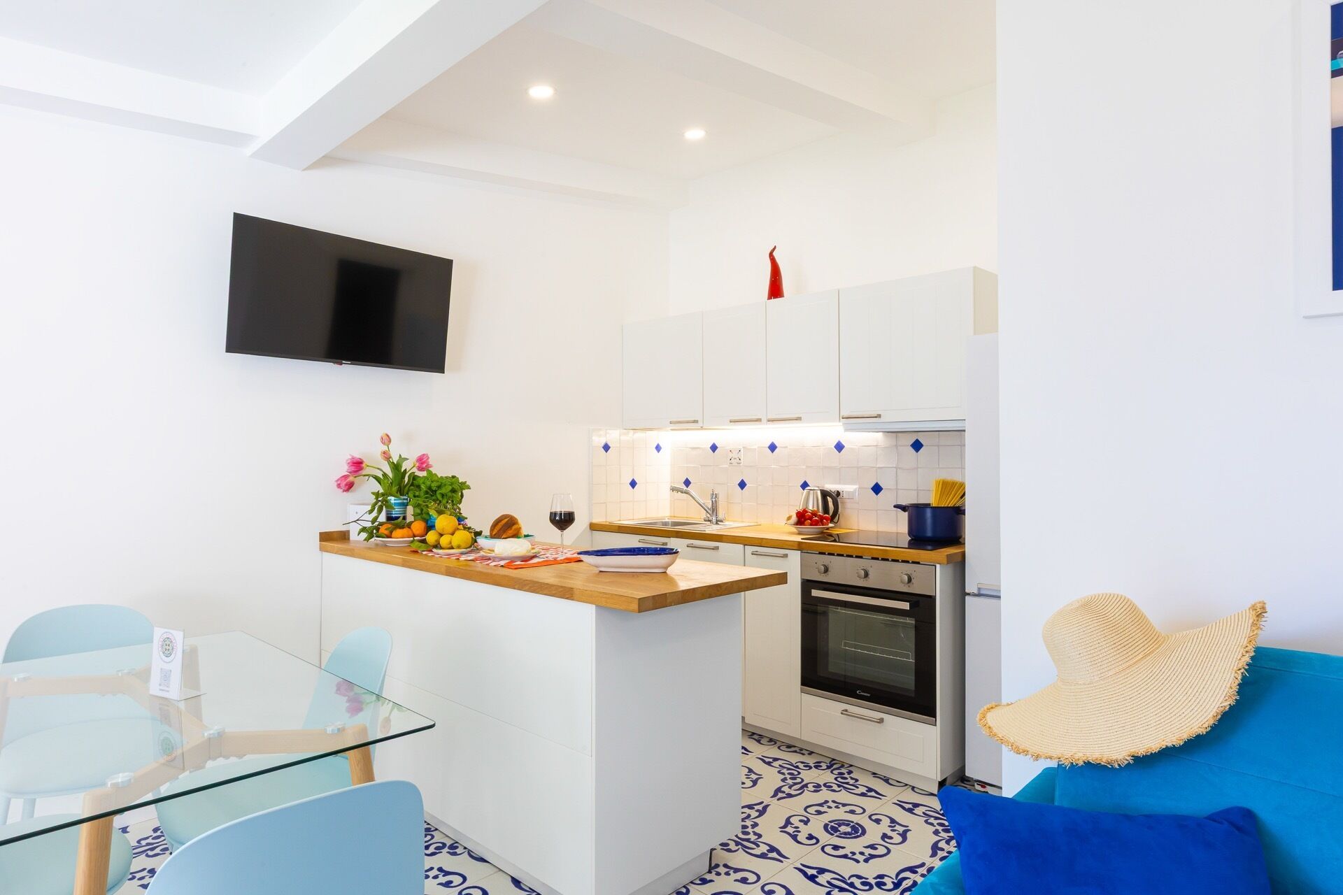Una cucina compatta con TV, una zona pranzo con tavolo in vetro e un divano blu.