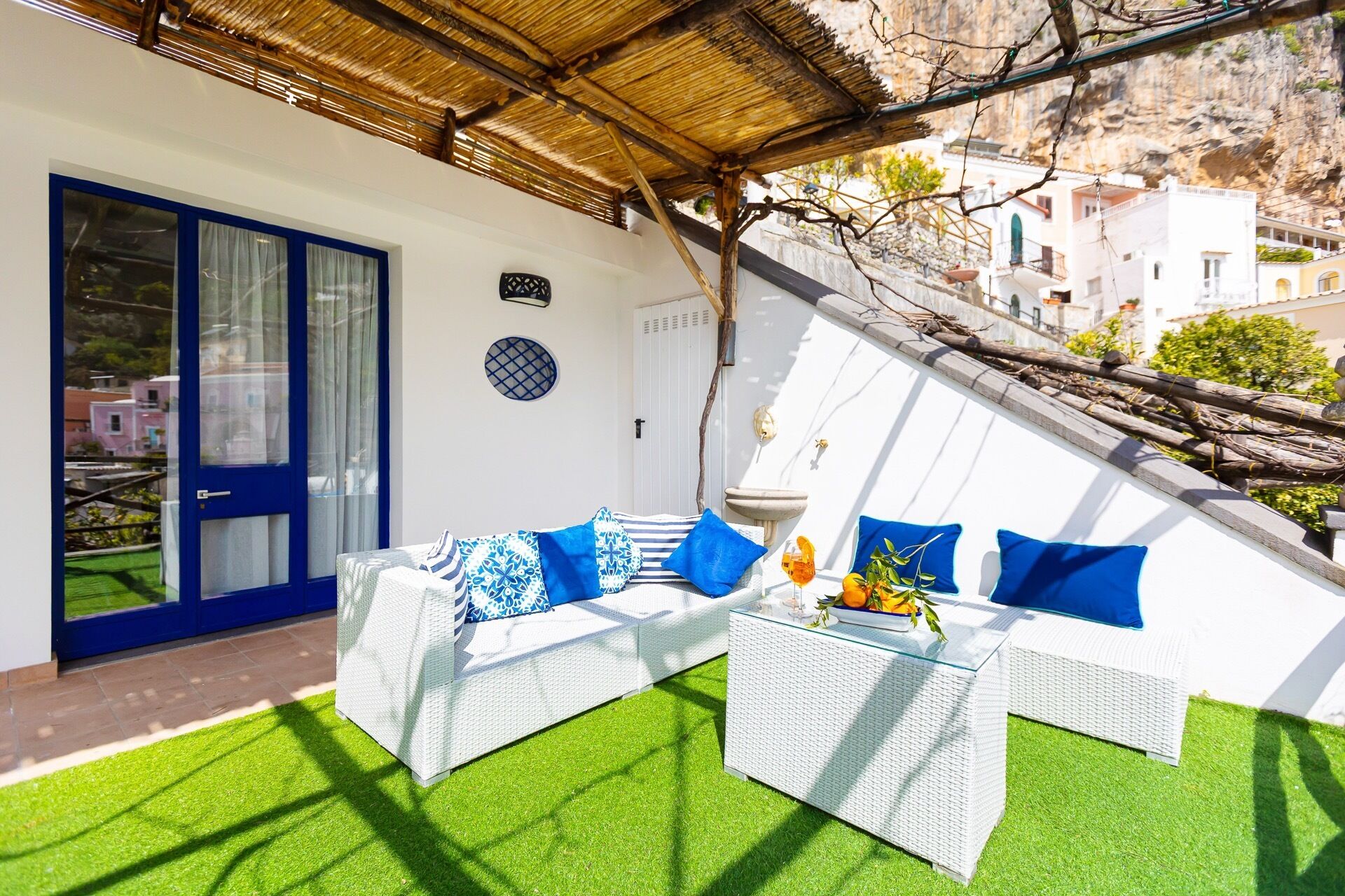 A room with a white sofa, blue cushions, a glass coffee table, and a view of a mountainous landscape.