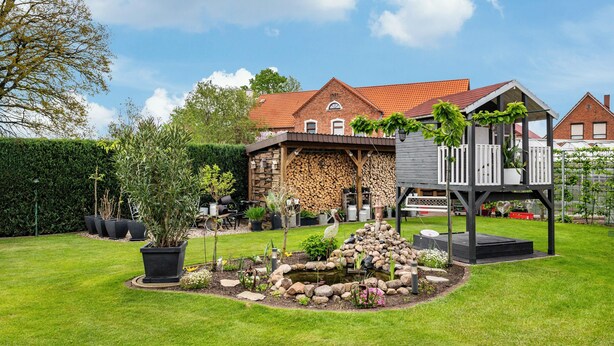 A residential property with a garden, a wooden deck, and a brick house with a red-tiled roof. - Apartment 'Für 6 Personen 90 M²' with Private Terrace, Shared Garden and Wi-Fi (Siggelkow)