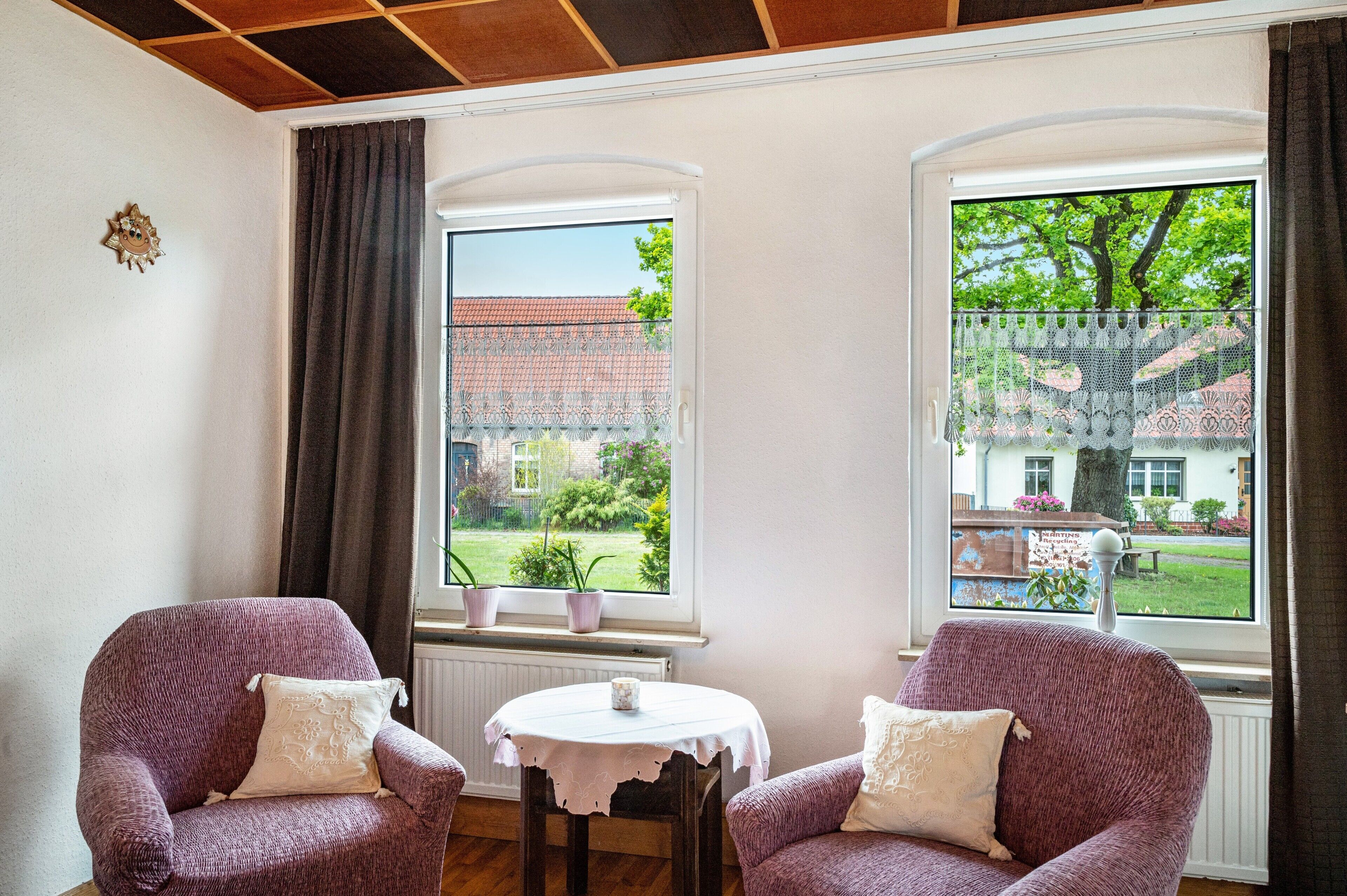 A room with two armchairs, a small table, and two windows with curtains.