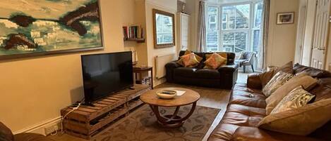 A living room with a sofa, a coffee table, a television, and a painting on the wall.