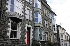 Un bâtiment en pierre à plusieurs étages, doté de fenêtres à encadrement blanc et d’une porte rouge.