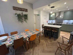 Cozinha moderna com ilha central, cadeiras de madeira e mesa de jantar com toalha de mesa estampada.