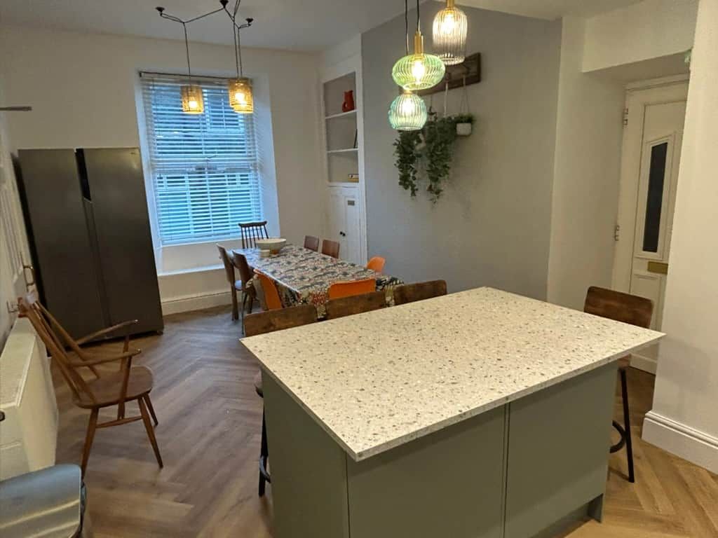 A kitchen with a central island, wooden chairs, and a dining table with chairs.