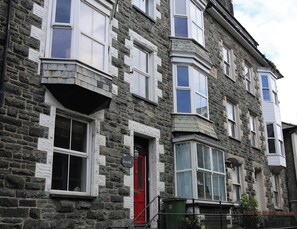 Un immeuble en pierre de plusieurs étages, avec des fenêtres à cadre blanc, une porte rouge et une enseigne sur laquelle on peut lire « Roschill ».