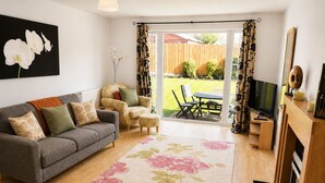 A living room with a sofa, armchair, TV, and a view of the backyard. - Modern, Spacious 6BR Gated Home - Sleeps 9 - Private Drive (Newcastle-under-Lyme)