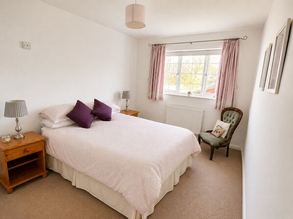 A bedroom with a bed, two bedside tables, a chair, a window with curtains, and a radiator.