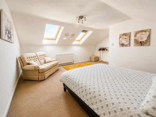 Een slaapkamer met een bed, een bank, een radiator, een geel vloerkleed en dakramen.