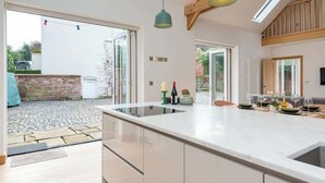 A modern kitchen with a large island, wooden beams, and a view to the outside. - 2 Bed Converted Barn (Ombersley)