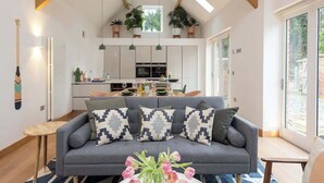 A modern living room with a grey sofa, decorative pillows, a vase of flowers, and a wooden ceiling. - 2 Bed Converted Barn (Ombersley)