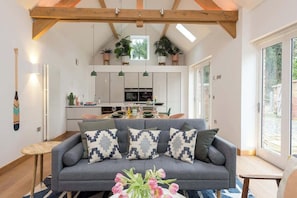 A modern living room with a grey sofa, decorative pillows, a vase of flowers, and a wooden ceiling. - 2 Bed Converted Barn (Ombersley)