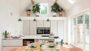 A modern kitchen with white cabinets, a dining table set for four, and hanging plants. - 2 Bed Converted Barn (Ombersley)