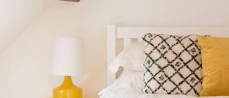A bed with patterned pillows, a white headboard, and a yellow bedside table with a lamp.