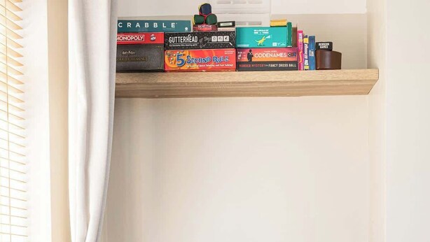 Een woonkamer met een bank, een stapel houtblokken, een boekenkast vol boeken, en een raam met gordijnen.