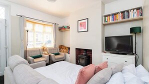 Een slaapkamer met een bed, een televisie, een open haard, een boekenkast en een raam met gordijnen.