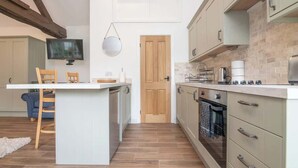 A compact kitchen with a central island, a television mounted above it, and a wooden door in the background. - Charming Warwickshire Studio (Wootton Wawen)