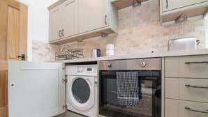 A compact kitchen with a washing machine, oven, and a coffee maker on the countertop. - Charming Warwickshire Studio (Wootton Wawen)