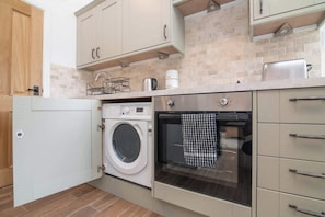 A compact kitchen with a washing machine, oven, and a coffee maker on the countertop. - Charming Warwickshire Studio (Wootton Wawen)