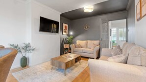 A living room with a sofa, coffee table, and a plant. - Cosy 3 Bed with Parking (Rugby)