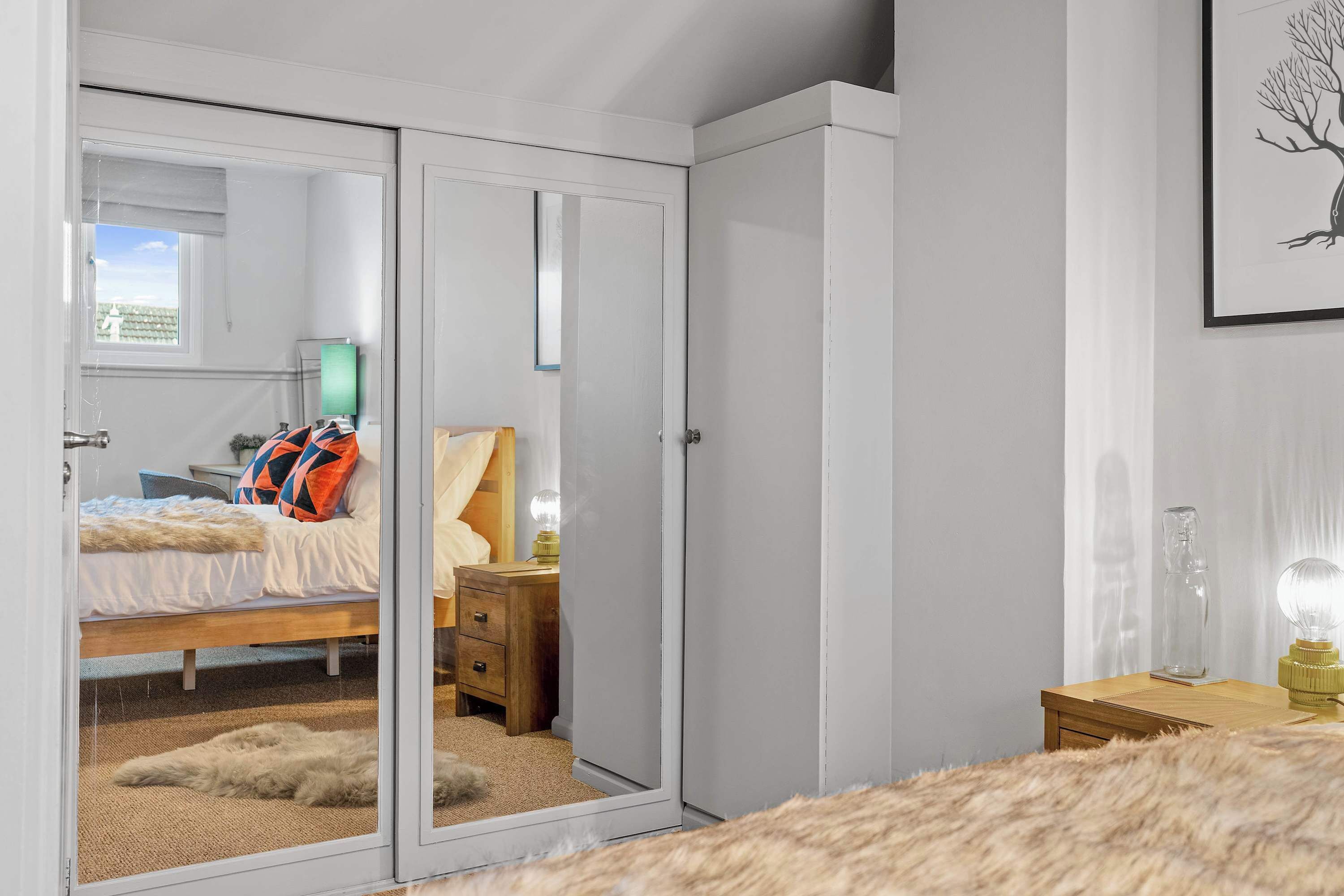 A bedroom with a bed, a wardrobe, a nightstand, and a lamp.