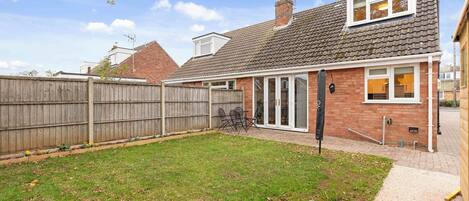 A residential backyard with a wooden fence, a grassy lawn, and a brick house with a tiled roof.