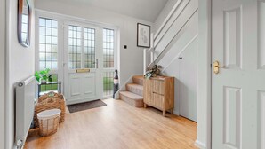 A hallway with a wooden floor, white doors, a staircase, and a wicker basket. - Cosy 3 Bed with Parking (Rugby)