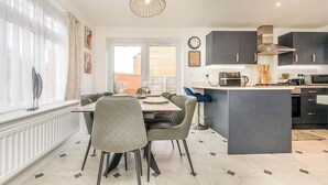 A modern kitchen with a dining area, large windows, and a view of the outside. - Leamington Spa Retreat - Garden - Parking - 5 mins (Royal Leamington Spa)
