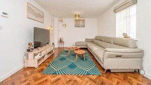 A living room with a sofa, TV, wooden entertainment unit, and a patterned rug. - Leamington Spa Retreat - Garden - Parking - 5 mins (Royal Leamington Spa)