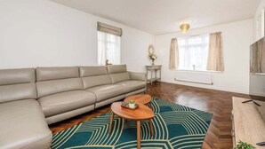 A living room with a sofa, a coffee table, a TV, and a small side table with a plant. - Leamington Spa Retreat - Garden - Parking - 5 mins (Royal Leamington Spa)