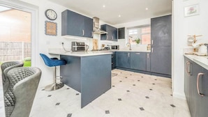 A modern kitchen with dark cabinets, a central island, and a bar stool. - Leamington Spa Retreat - Garden - Parking - 5 mins (Royal Leamington Spa)