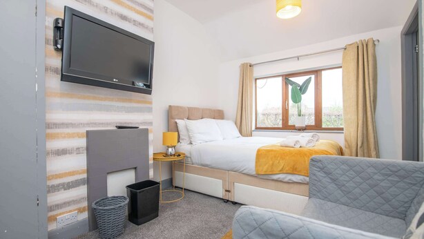 Camera d'albergo con un letto, una TV a parete, un comodino con una lampada, una finestra con tende e vista esterna.