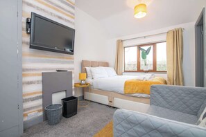 Une chambre d’hôtel avec un lit, un téléviseur fixé au mur, une table de chevet avec une lampe, une fenêtre avec des rideaux et une vue sur l’extérieur.