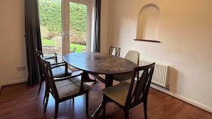 A dining area with a round table and four chairs, a radiator, and a window with curtains.