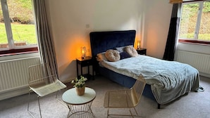 A bedroom with a bed, two chairs, a small table, and a bedside lamp.