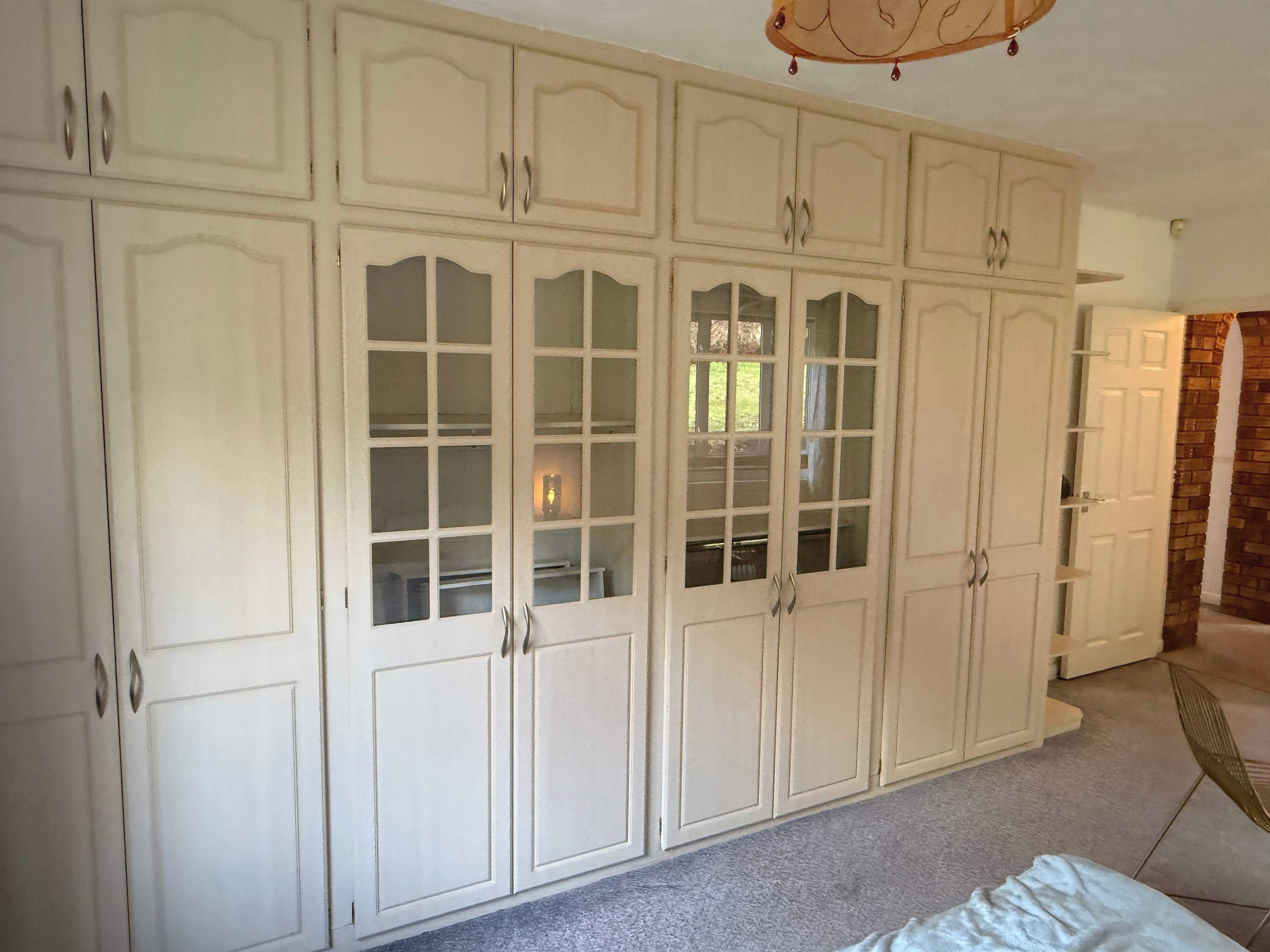 A room with a large white wardrobe, a bed, and a chair.