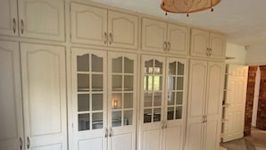 A room with a large white wardrobe, a bed, and a chair.